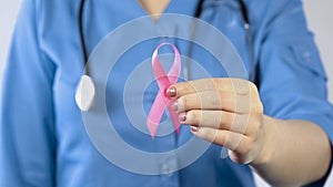 Female doctor holding pink ribbon close up, breast cancer awareness symbol