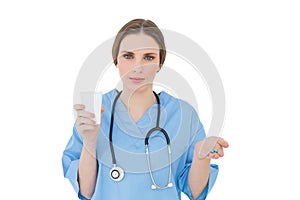 Female doctor holding a plastic cup and pills while looking into the camera