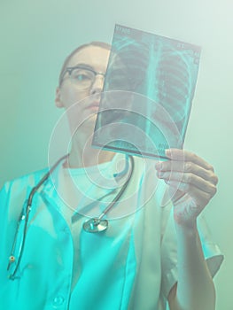 Female doctor holding X-ray of lungs, fluorography, roentgen in hospital. Woman in medical gown, stethoscope in consulting room.