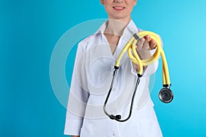Female doctor holding stethoscope on color background, closeup view with space for text.