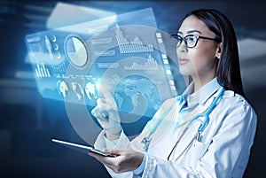 Female doctor holding a tablet computer and touching medical graphs on virtual screen