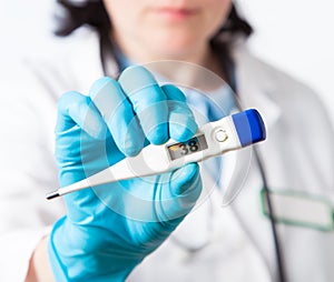 Female doctor holds a electronic thermometer for measuring temperature, closeup.  nurse measures the temperature. Shallow depth of