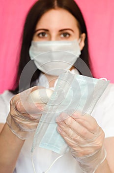 Female doctor holds a piece of soap and a medical mask on pink background. Prevention of different viral illnesses including covid