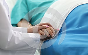 Female doctor holds sick man hospital bed by hand