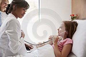 Female Doctor Letting Girl Patient Listen To Her Chest With Stethoscope In Hospital Bed