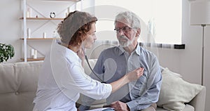Female doctor listening old patient with stethoscope during homecare visit