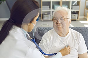 Female doctor listening to white-haired male patient`s heart through stethoscope photo