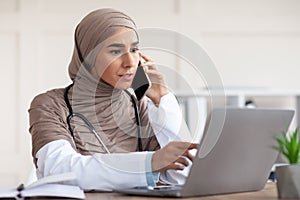 Female doctor looking at laptop screen and talking on phone