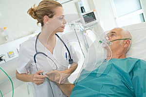 Female doctor looking at senior male patient wearing oxygen mask