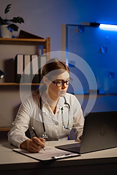 Female doctor make online video call consult patient on laptop while working at night shift. Medical assistant young