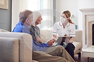 Female Doctor With Mask Makes Home Visit To Senior Couple For Medical Check During Covid-19 Lockdown