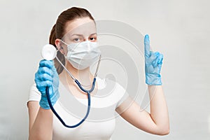 Female doctor in mask with a stethoscope shows a finger to the side