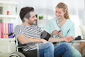 female doctor measuring blood pressure to disabled young man
