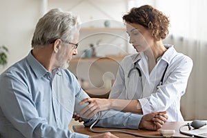 Female doctor measuring senior patient blood pressure at hospital