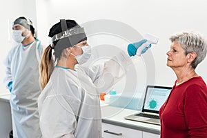 Female doctor measuring senior patient temperature for coronavirus disease - Focus on right woman