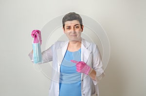 Female doctor in medical gown holds one-off mask in her hand, disgustedly pointing her finger at it