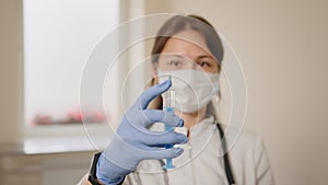 Female doctor with medical mask and gloves prepares prefilled syringe for injection by removing cap, tapping the syringe