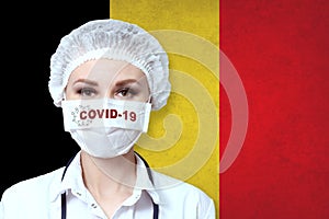 Female doctor in medical mask with the inscription COVID-19 on a blurred background of the flag of Belgium. Pandemic virus COVID-
