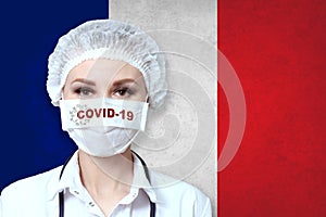 Female doctor in medical mask with the inscription COVID-19 on a blurred background of the flag of France. Pandemic virus COVID-19