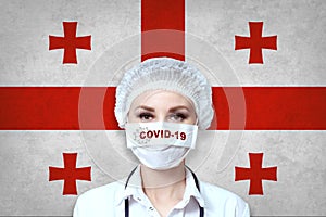 Female doctor in medical mask with the inscription COVID-19 on a blurred background of the flag of Georgia. Pandemic virus COVID-