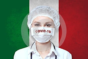 Female doctor in medical mask with the inscription COVID-19 on a blurred background of the flag of Italy. Pandemic virus COVID-19