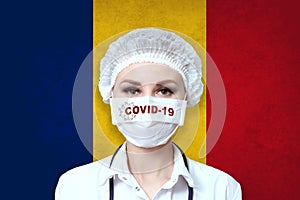 Female doctor in medical mask with the inscription COVID-19 on a blurred background of the flag of Romania. Pandemic virus COVID-