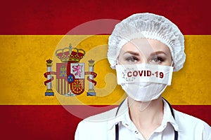 Female doctor in medical mask with the inscription COVID-19 on a blurred background of the flag of Spain. Pandemic virus COVID-19