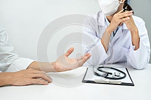 A female doctor in medical mask is listening symptom from patient during discussing about diagnosis of disease