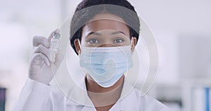 A female doctor in a medical mask and rubber gloves holds a small ampoule containing the covid-19 vaccine in her hands