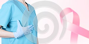 A female doctor in a medical uniform supports her breasts and a pink ribbon as a symbol of breast cancer awareness. Medical pink