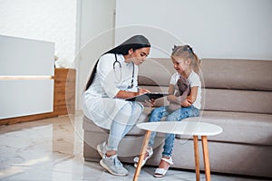 Female doctor with notepad sits in the clinic with little girl