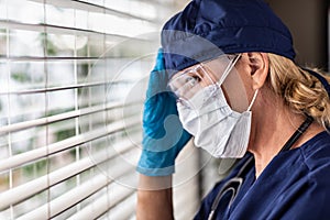 Female Doctor or Nurse On Break At Window Wearing Medical Face Mask and Goggles