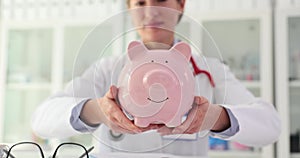 Female doctor nurse holding pink piggy bank in clinic