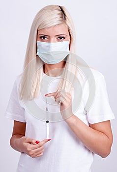 Female doctor or nurse in medical mask holding syringe with injection