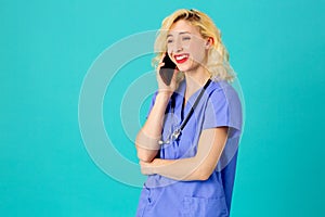 Female doctor or nurse wearing blue scrub uniform and stethoscope talking on mobile phone