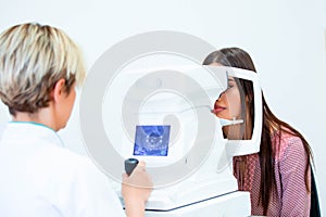 Female doctor ophthalmologist is checking the eye vision of attractive young woman in modern clinic. Doctor and patient in