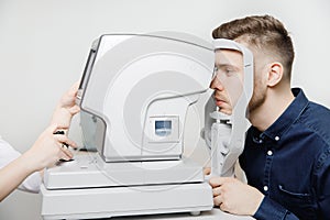 Female doctor ophthalmologist clinic checks eye vision of man on machine lamp.