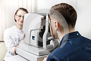 Female doctor ophthalmologist clinic checks eye vision of man on machine lamp.