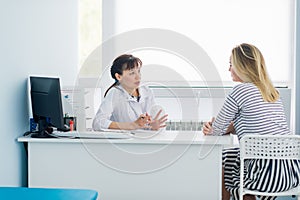 Female doctor and patient talking in hospital office. Health care and client service in medicine