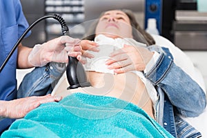 Female doctor performing radiofrequency lifting procedure on abdomen of mature woman