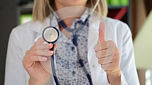 Female doctor posing in clinic office showing stethoscope and thumb up sign