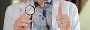 Female doctor posing in clinic office showing stethoscope and thumb up sign