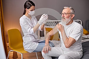 Female Doctor Preparing Syringe For Making Injection To Elderly Man