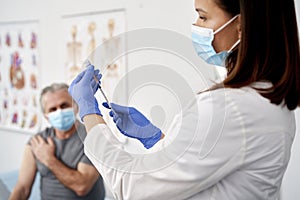 Female doctor preparing syringe for senior patient