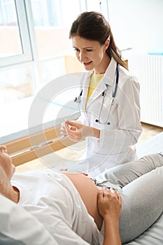 Female doctor preparing syringe to injection and looking at pregnant woman