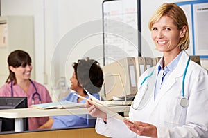 Female Doctor Reading Patient Notes At Nurses Station