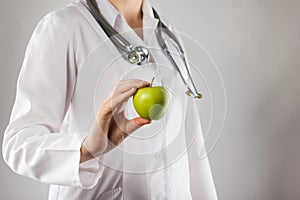 Female doctor's hand holding green apple. Close up shot on grey