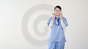 A female doctor in scrubs stands against an isolated white background with her stethoscope