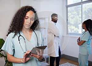 Female doctor in scrubs uses digital tablet with medical team in background