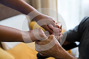 Female doctor and senior man holding hands in nursing home